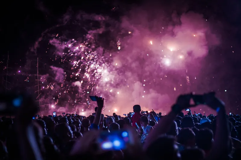 Back view of a crowd recording a live performance on cellphones in a concert hall lit by shiny spotlights.