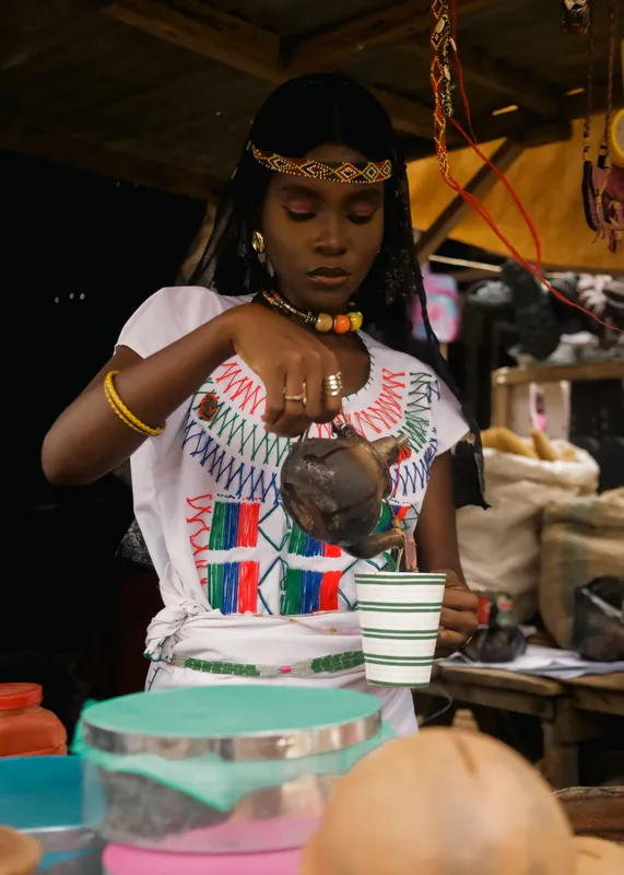 Young woman in traditional Ethiopian attire pouring coffee during a cultural ceremony.