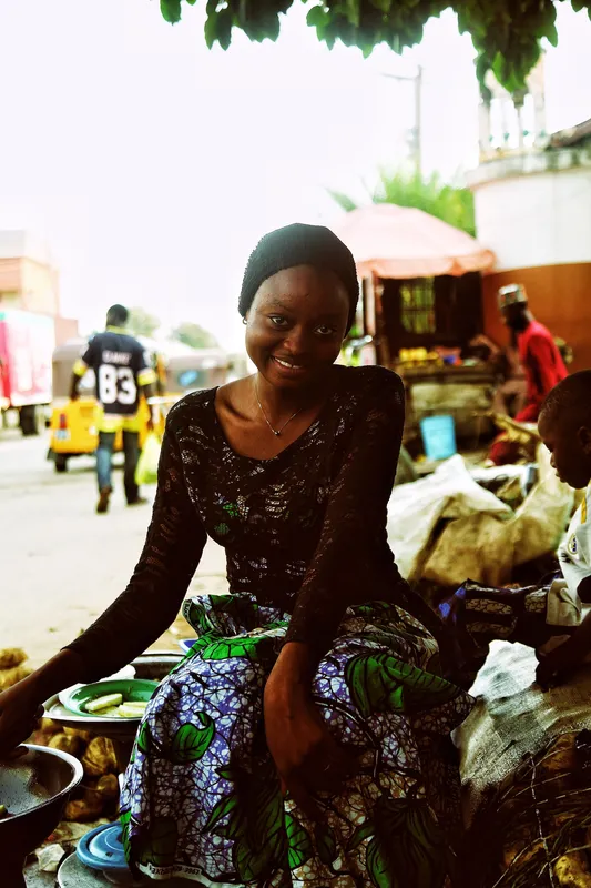 A smiling woman at her stall in an Abuja street market.