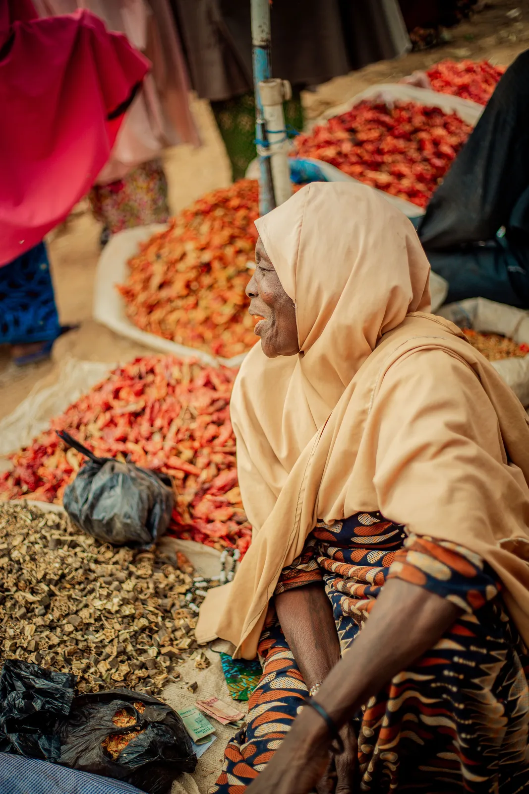 Elderly woman in a spice market with colorful dried peppers.