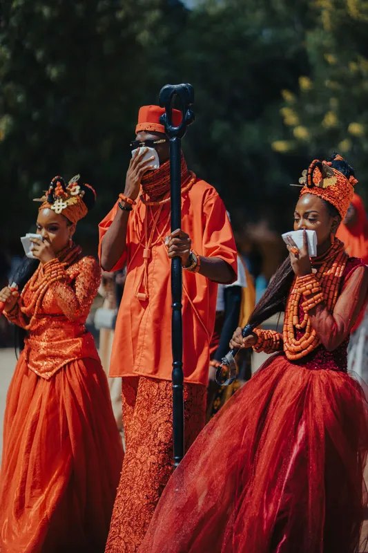 Three adults in vibrant traditional attire during an African wedding celebration.